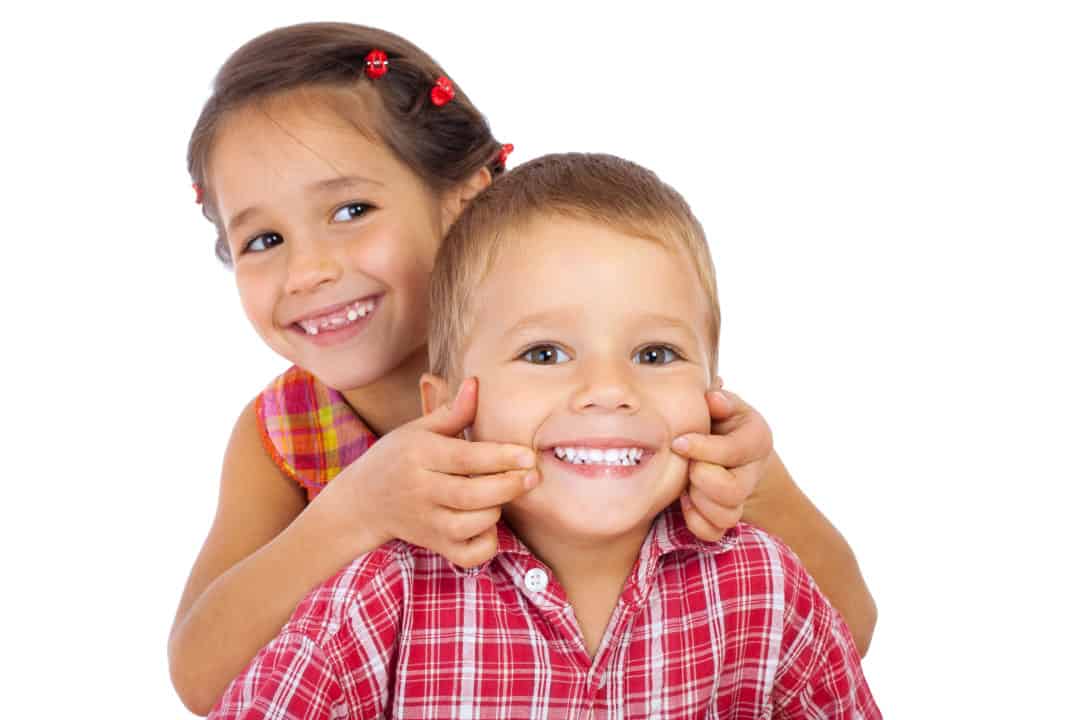 Two funny smiling little children, showing their teeth, isolated on white