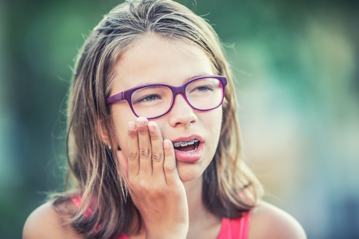 a little girl with braces wearing glasses and making a face to show tooth pain