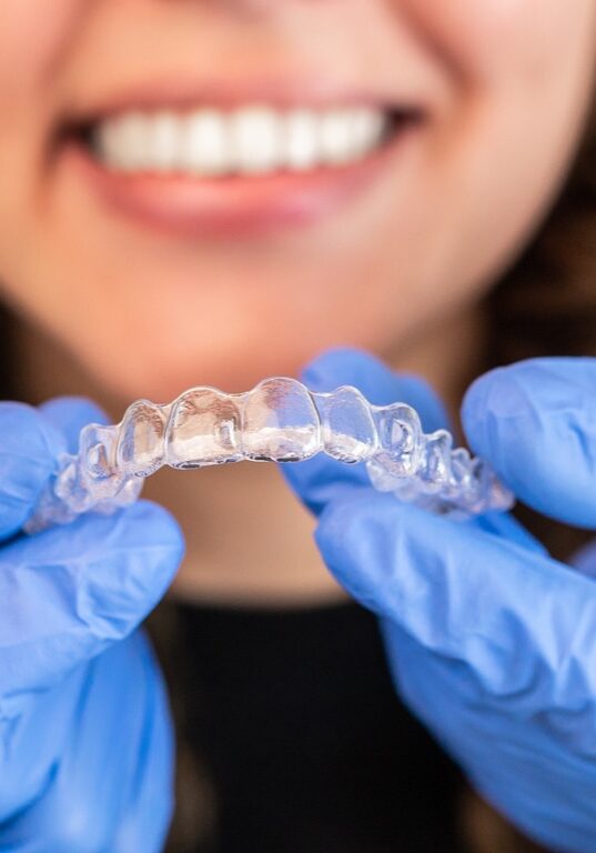 Orthodontist doctor in gloves putting silicone invisible transparent braces on woman's teeth in dentist clinic, mouth closeup view. Correcting teeth treatment and cure in dentistry.