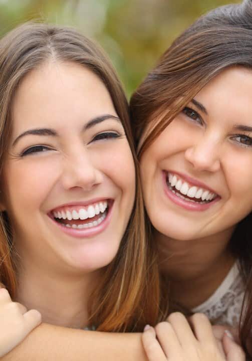 Two women friends laughing with a perfect white teeth with a green background