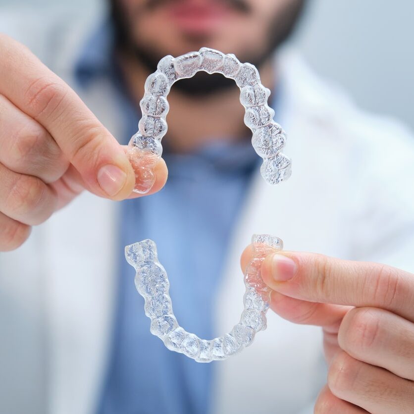 A young orthodontist holding Invisalign dental retainers.