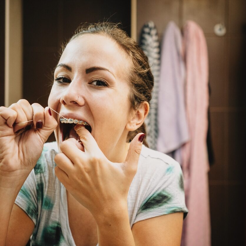 Woman cleaning her teeth's with dental floss in bathroom