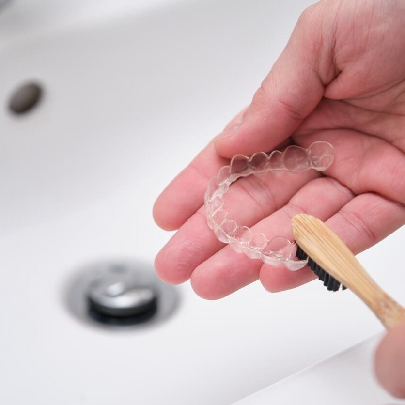 a person cleaning an invisalign tray in their hand with a toothbrush