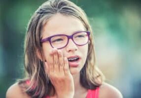 a little girl with braces wearing glasses and making a face to show tooth pain
