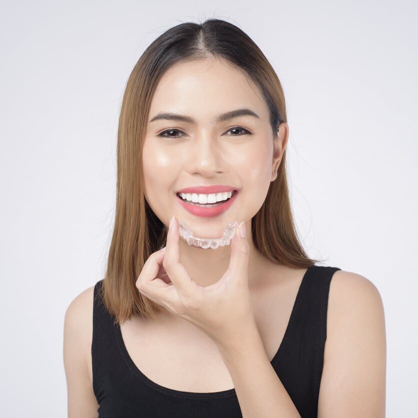 Young smiling woman holding invisalign braces